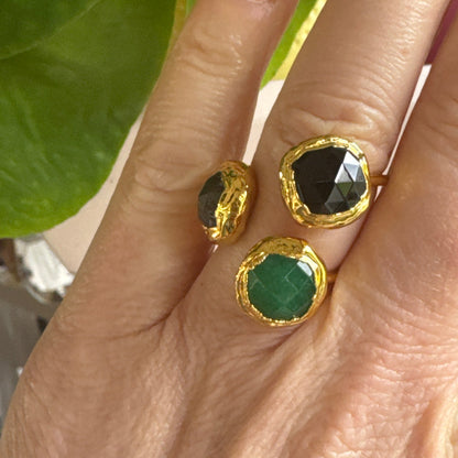 Gold rings with green and black gemstones on a hand with green leaves in the background